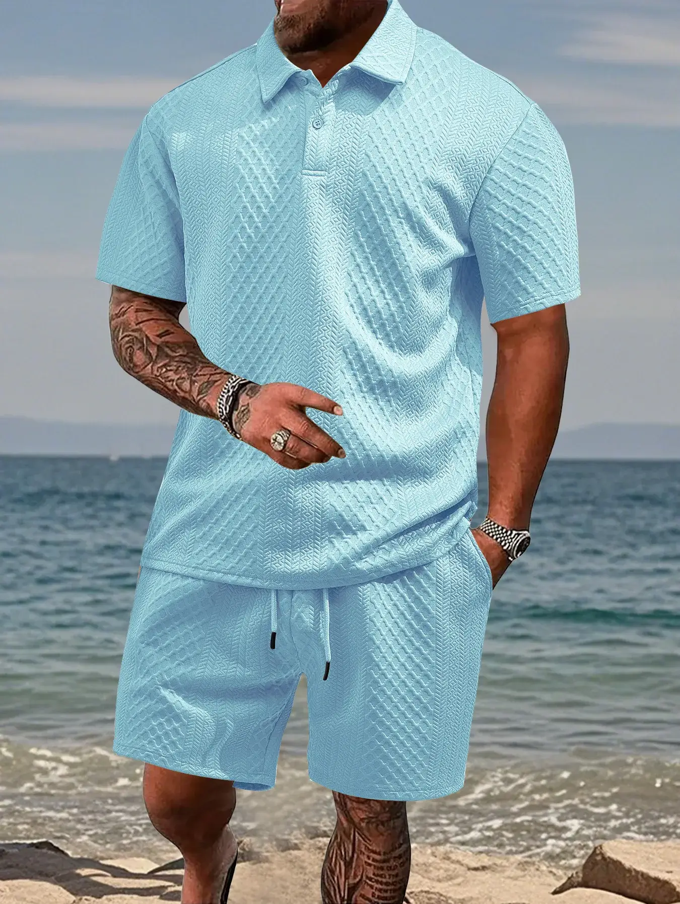 Man in light blue casual outfit standing on the beach.