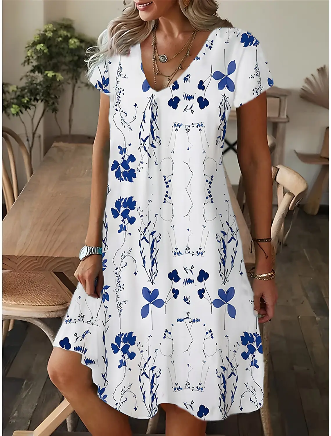Woman in a white dress with blue floral prints standing indoors.