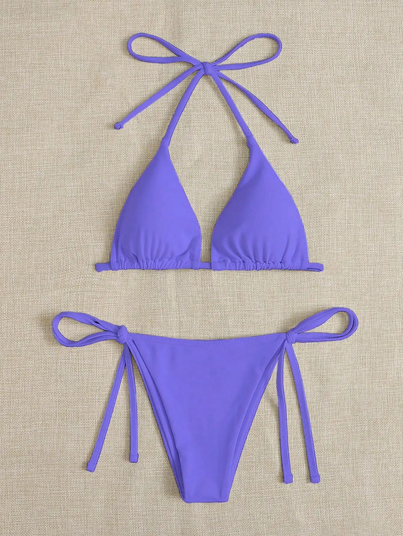 Purple two-piece bikini with tie straps on a beige background.