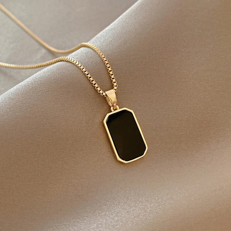 Gold necklace with black rectangular pendant.