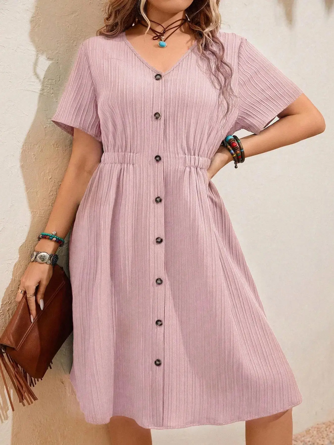 Woman in a pink button-down dress holding a brown bag.