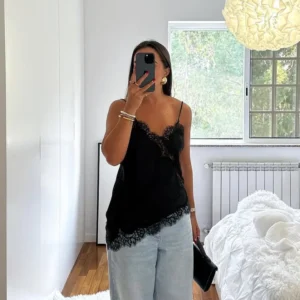 Woman in casual black lace top and light jeans taking mirror selfie.