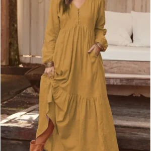 Woman wearing a long mustard yellow dress with pockets and long sleeves.