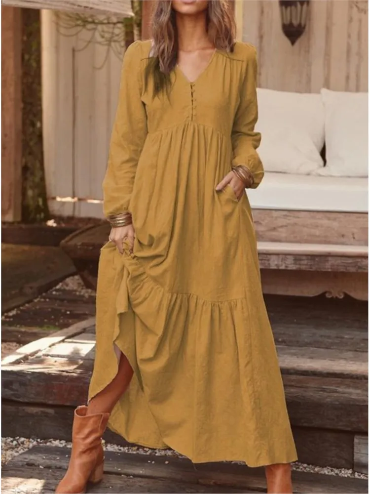 Woman wearing a long mustard yellow dress with pockets and long sleeves.