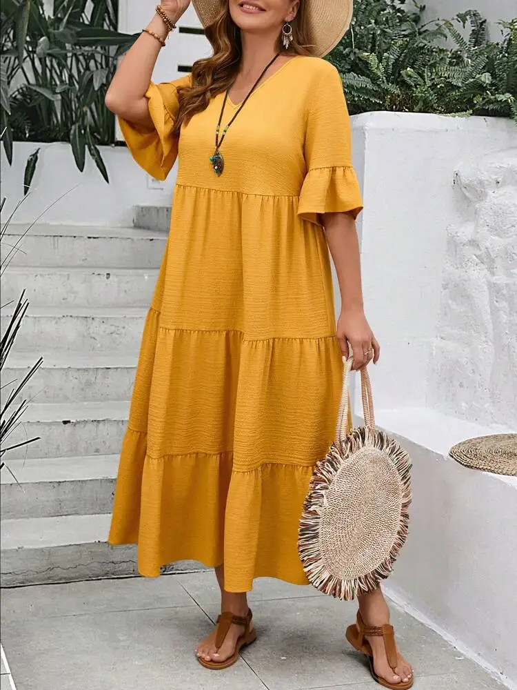 Woman in a mustard yellow tiered dress holding a round straw bag.