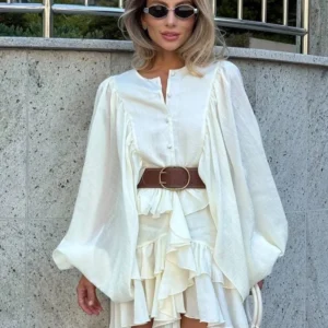 Woman wearing a flowing white dress with a brown belt and sunglasses.