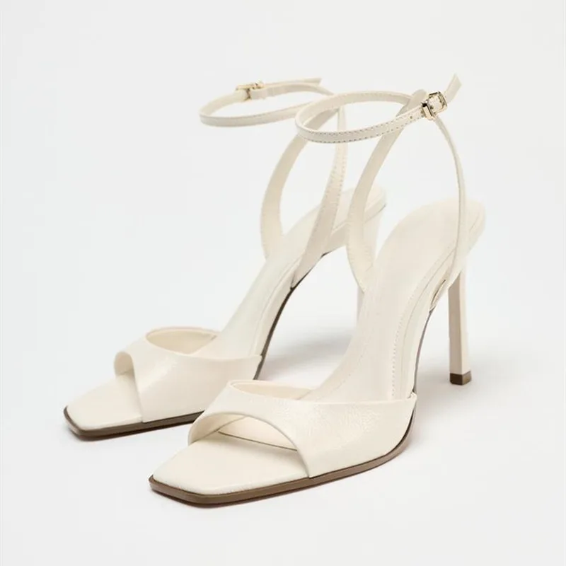 Elegant white high-heeled sandals with ankle straps and square toes.