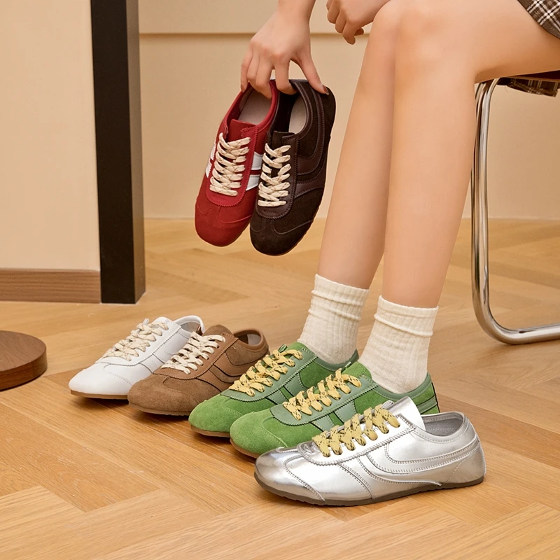 Person holding two pairs of sneakers with three more pairs on the floor.