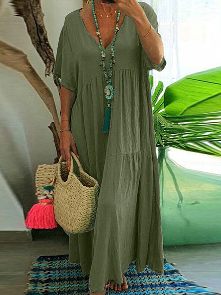 Woman in a loose green dress holding a woven straw bag.