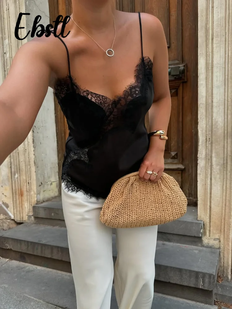 Woman wearing a black lace camisole and white pants, holding a textured beige clutch.