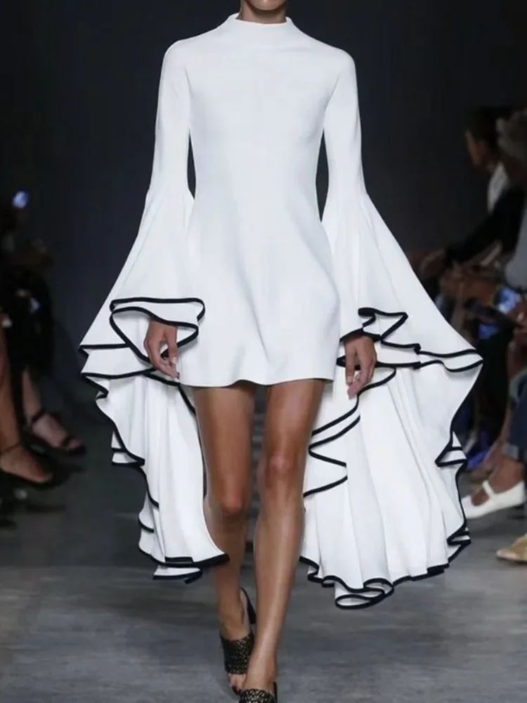 Model walking runway in white asymmetrical dress with black trim details.