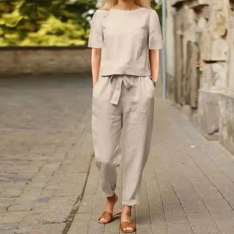 Woman walking in beige casual outfit on a cobblestone path.