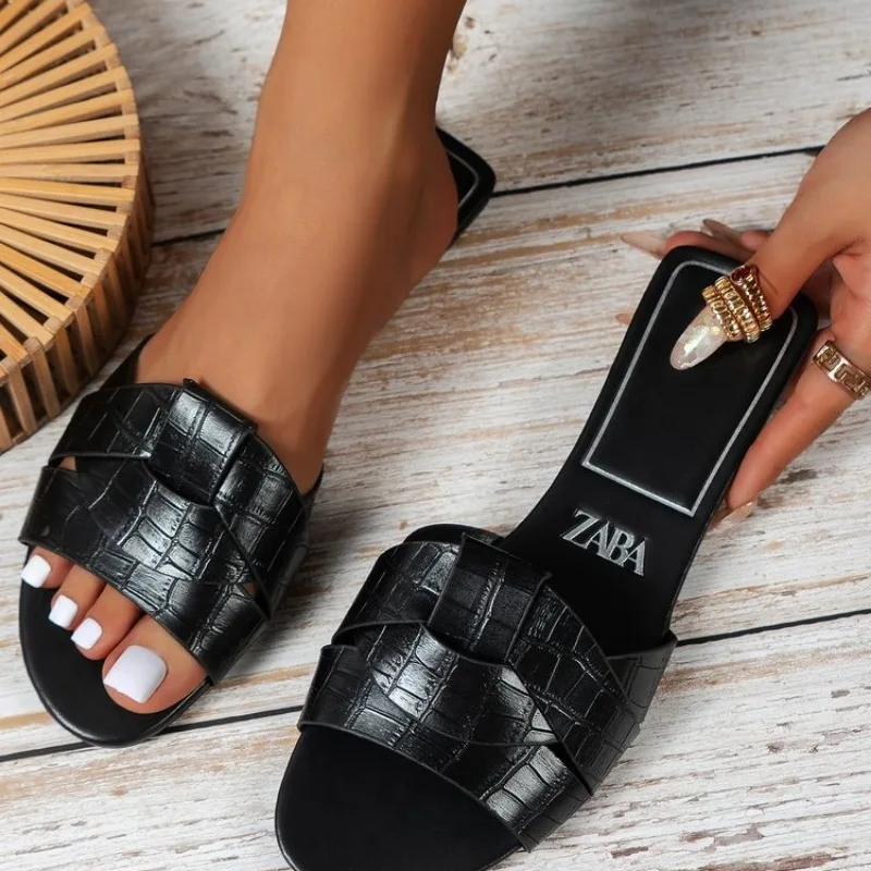 Black woven design slip-on sandals with white painted toenails.