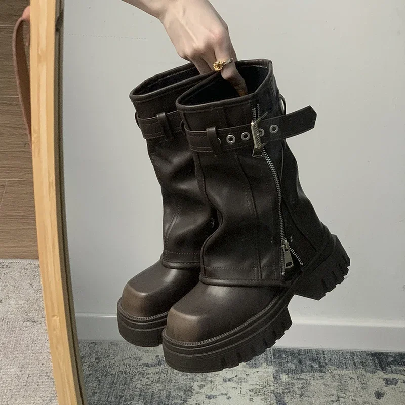 Person holding a pair of chunky black boots with buckles.