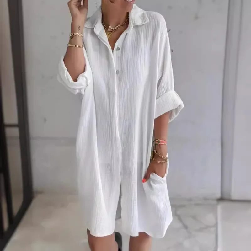 Woman wearing a loose white shirt dress with rolled-up sleeves.