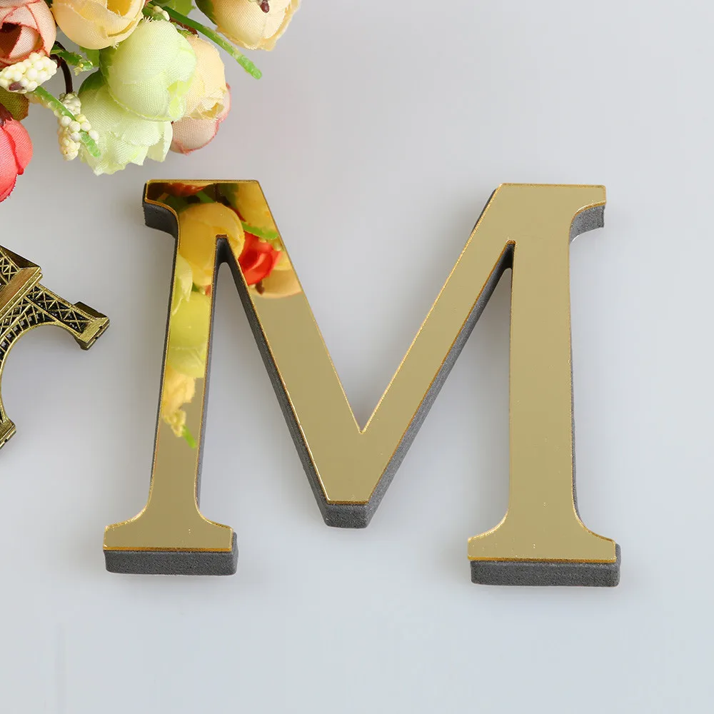 Gold letter 'M' decoration on a white surface with flowers.